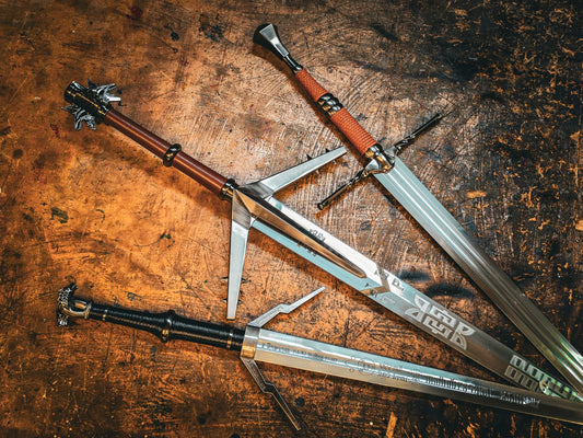 Three fantasy sword replicas laid out on a workshop bench