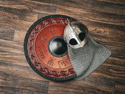 Viking round shield with carved runes beside a riveted helmet and chainmail aventail